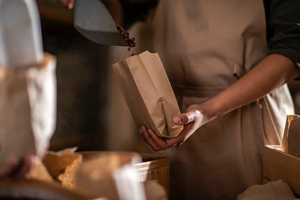 istock Worker Filling Paper Bag with Coffee Beans in Rustic Setting 2240106097