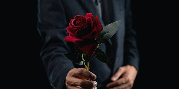 istock Elegant Man Presenting Red Rose in Dark Setting for Romantic Gesture 2240107916