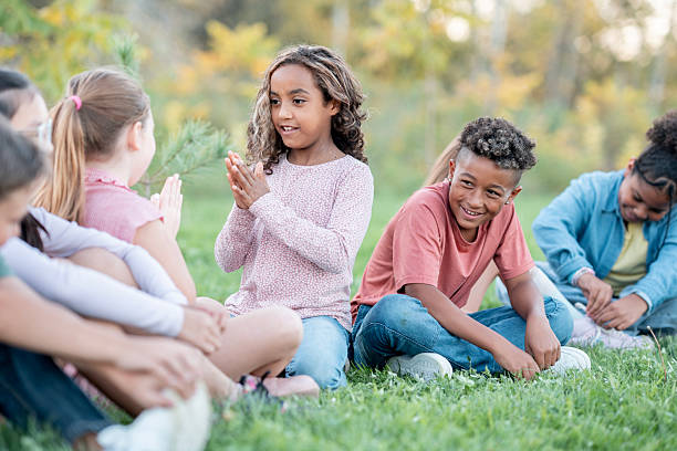 istock Diverse Group Of Children Sitting On Grass Outdoors, Smiling And Clapping Hands Together 2240108288