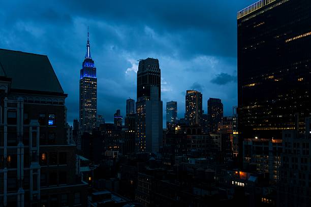 Night view of New York City skyline with illuminated skyscrapers and cloudy sky.