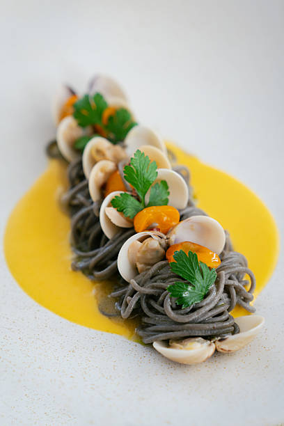 Black squid ink pasta with clams, yellow sauce, and fresh herbs in a fine dining restaurant