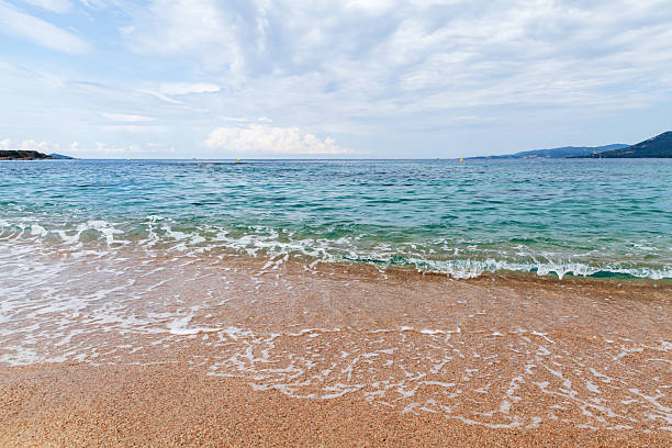 Shore water covers sandy beach of Propriano under cloudy blue sky on a summer day. Coastal landscape of Corsica, France