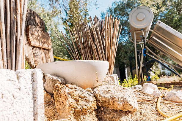 White ceramic bowl on rocks in a rustic outdoor garden with dried sticks and solar panels nearby. Eco-friendly solar energy setup in a natural, sunny garden environment.