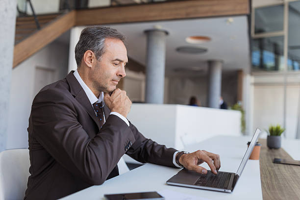 istock Mature businessman thinking while typing on laptop in modern office 2240114505