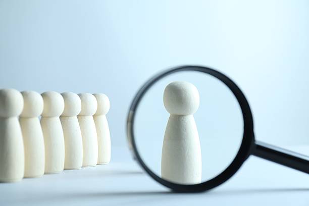 istock Human resources concept. Looking at wooden figure through magnifying glass on light background, closeup 2240117574