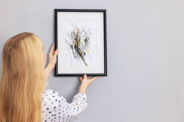 istock Female decorator hanging abstract picture indoors, back view. Space for text 2240118233