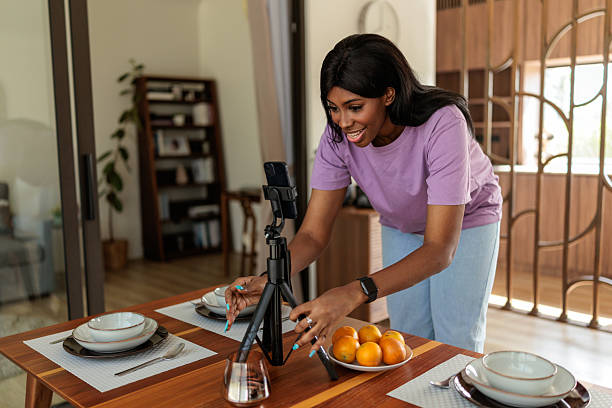 istock Smiling Woman Adjusting Smartphone On Tripod While Recording At Home 2240120241