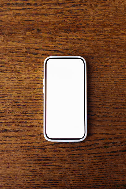 Top view of smartphone with white blank screen on wooden table. Minimalist workspace with flat lay composition, perfect for adding text or design mockups.