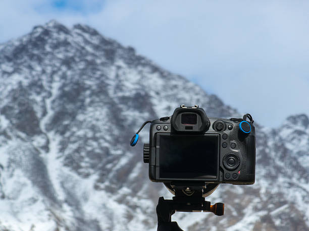 Camera takes a picture of majestic mountains in the background. The outdoor scene conveys a peaceful and serene mood, highlighting the beauty of nature.