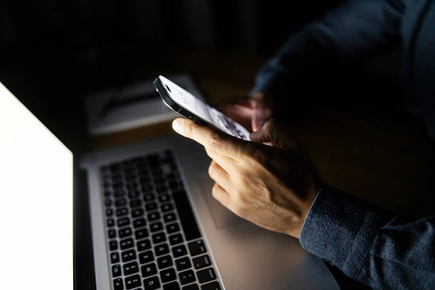 istock Person browsing phone in dark with laptop screen light 2240141805
