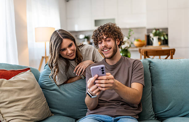 istock Couple relaxing on sofa at home browsing smartphone 2240142291