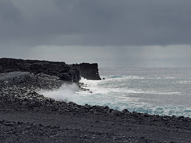 Pahoa, Hawaii Island, Hawaii, USA - July 15, 2025: Pohoiki Black Sand Beach landscape with white surf  crashing ocean waves under heavy dark gray cloudscape