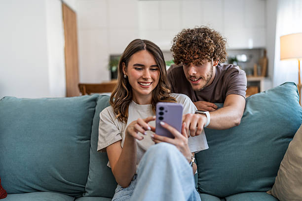 istock Young couple enjoying smartphone content together on sofa at home 2240143289