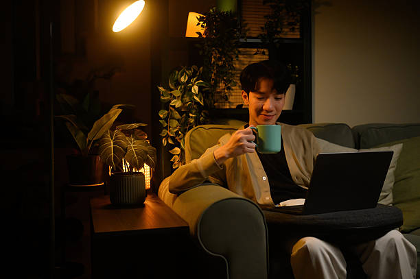 istock Calm home workspace scene of a man using a laptop at night while sipping coffee in cozy lighting 2240144248