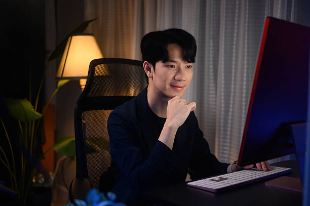 istock Confident man in a blazer smiles while working on a desktop at night, representing dedication, productivity, and a positive work attitude 2240145328