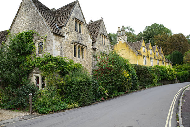 Charming stone cottages line a street in Castle Combe, Great Britain, within the Cotswolds. The older Cotswold stone buildings exhibit characteristic steeply pitched roofs and gable windows.