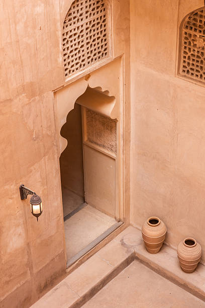 Traditional omani architecture features a decorative archway, patterned window, and terracotta pots in a courtyard