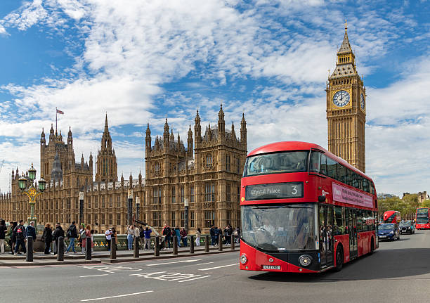 London, United Kingdom - April 19, 2025: A picture of an iconic red double-decker bus driving on the Westminster Bridge and in front of Big Ben and the Palace of Westminster.