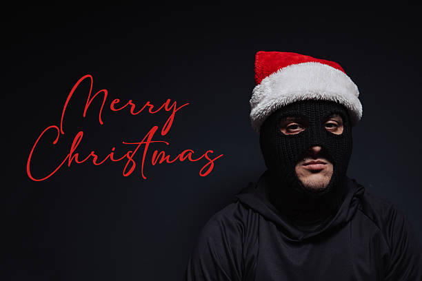 istock Masked robber and Christmas hat on a black background and Merry Christmas text 2240152276
