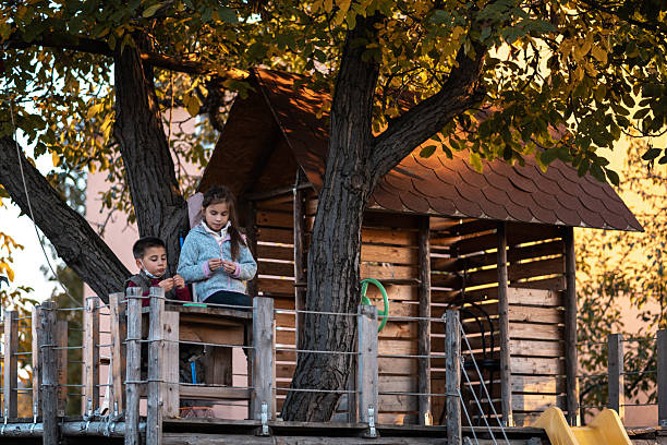 Two young children sitting and playing together in a wooden treehouse, enjoying the warm golden light of an autumn evening