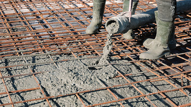 istock Concrete being poured over steel reinforcement mesh. Construction workers in boots pouring wet concrete onto a rebar grid, preparing the foundation slab for a building structure. 2240153266