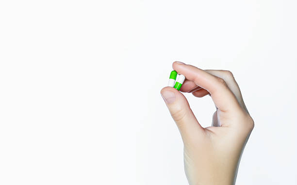 istock Hand holding two green and white capsule pills on white background 2240153427