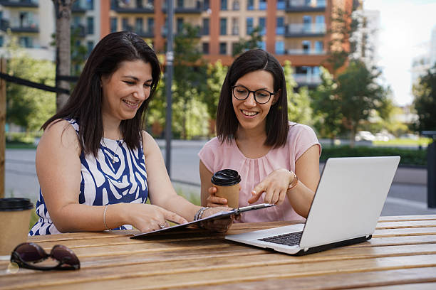 istock Two Young Women Working and Socializing Outdoors with Laptop and Coffee 2240153559