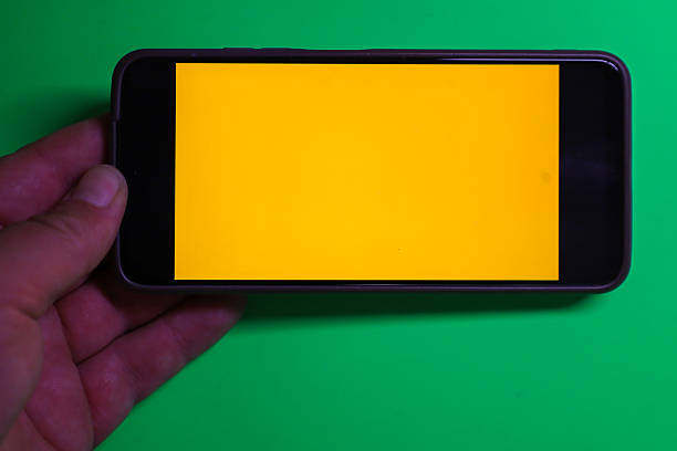 This horizontal shot shows a hand holding a smartphone with a bright yellow screen, positioned on a green background.