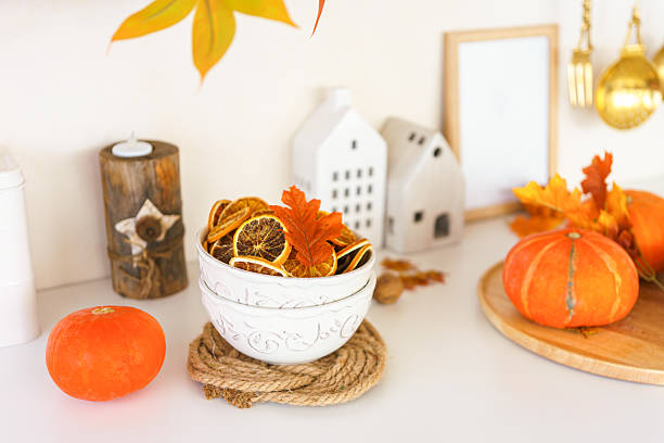 istock Autumn decoration with dried oranges, leaves, orange pumpkin in kitchen setting on white background 2240159434