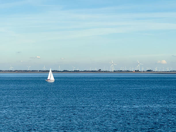 View over the Eastern Scheldt  with sailing boat and windmills in the distance in Wemeldinge, a village located in the province of Zeeland in the Netherlands.