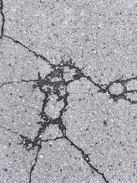 istock Intricate spiderweb pattern of cracks across gray asphalt road surface top view 2240161367
