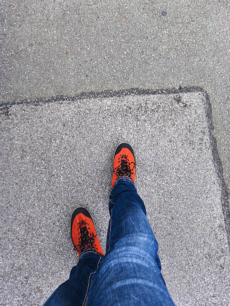 Bright orange hiking boots and denim jeans standing on asphalt pavement surface
