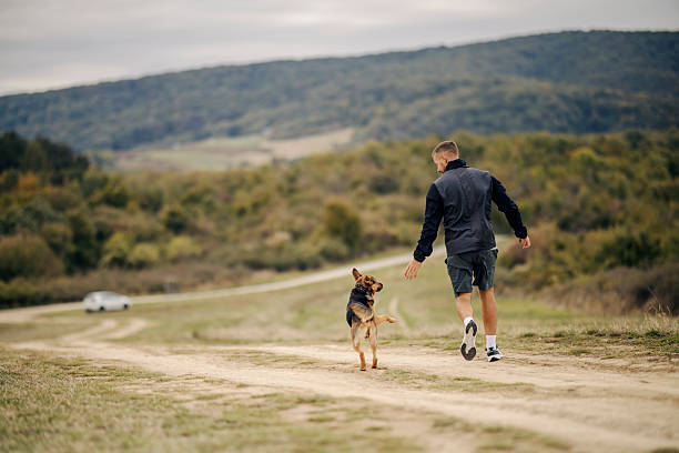 Young man running outdoors with his playful dog on a rural dirt road, enjoying nature and a healthy lifestyle