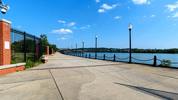 Washington, D.C., United States - September 3, 2023: View along the Anacostia Riverwalk Trail at Navy Yard, showing lamp posts and fencing beside the river. The public waterfront path is part of the Capitol Riverfront redevelopment.