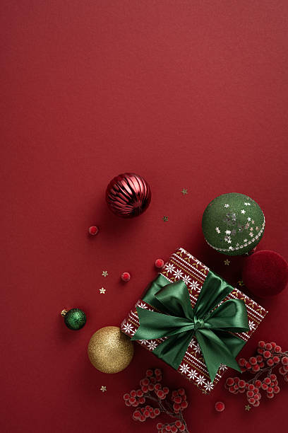 istock A rich vertical red background hosts a wrapped gift with green bow, plus ornaments, berries, and sparkle elements, evoking Christmas and New Year cheer, celebration, and warm holiday greeting 2240173066