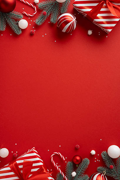 istock Vertical holiday scene with a red background featuring presents, ornaments, candy canes and evergreen branches 2240173076