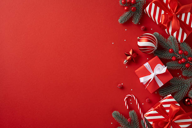 istock Bright red background with wrapped gift boxes, striped ornaments, candy canes, and green pine branches captures Christmas and New Year joy and warm holiday greeting mood 2240173113