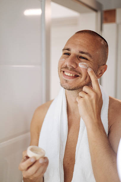 istock Smiling Man Applying Face Cream in Bathroom After Shower 2240173446
