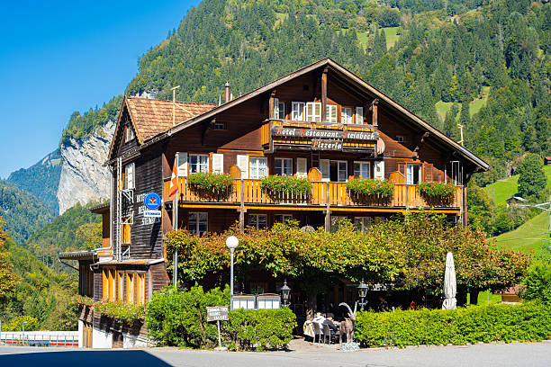 Lauterbrunnen, Switzerland - October 2, 2025: Charming wooden chalet-style hotel, resturant and pizzeria Steinbock with balconies, surrounded by lush green mountains and clear blue sky.