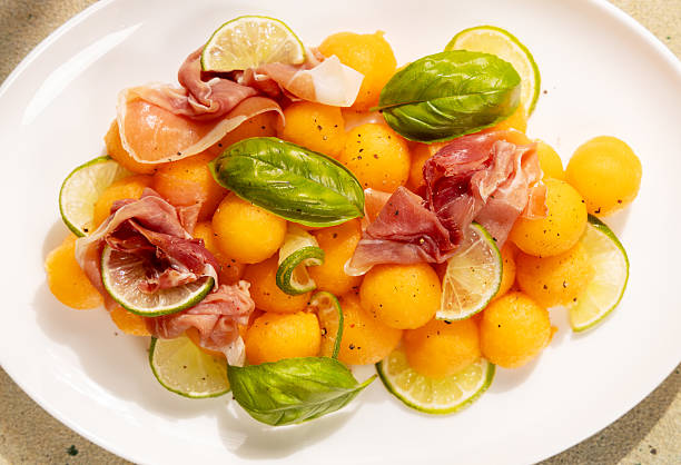 istock Melon prosciutto salad with fresh basil and lime on white plate 2240176339