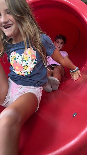 istock Action Image of Two Young Sisters Laughing and Having Fun Sliding Down Tunnel Slide 2240179990
