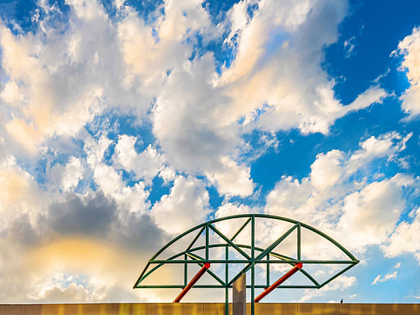 A green and red abstract structure at the top resembles a skeletal steel frame or scaffold-like grid, possibly intended as a visual marker or branding element. There is a lone pigeon on the roof's edge. The sky is filling with puffy clouds just beginning to turn golden during golden hour. This is from the top of a building in Adelaide Australia.