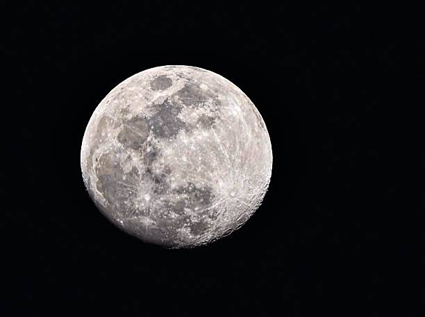 The moon in its waxing gibbous phase rises into the night sky showing off surface details.