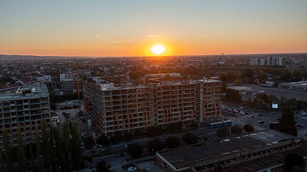 Sunset view of a large urban construction site with multiple buildings in progress surrounded by city infrastructure and roads during late evening in a suburban area.