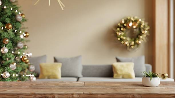 A blank wooden table foreground with a blurred Christmas-themed background, featuring a decorated tree and a gold wreath- 3D rendering