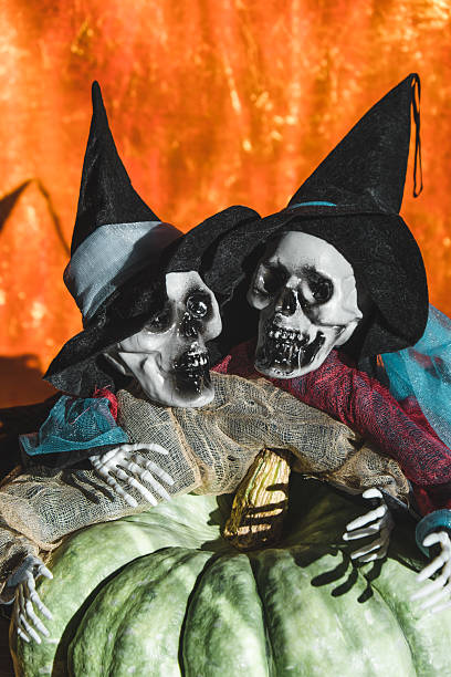 istock skeletal witches sit together on pumpkin during Halloween celebration vibrant orange background. 2240205346