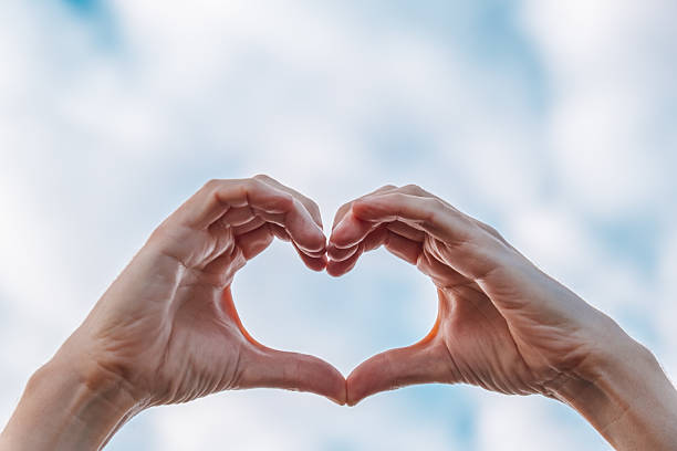 istock creating heart shape with hands against bright blue sky in peaceful outdoor setting. closeup. 2240206070
