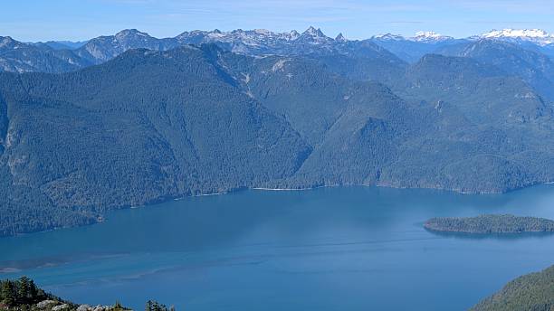 istock Pitt Lake surrounded by Forested Mountains, Snow-Capped Peaks, and Rocky Foreground Under Partly Cloudy Sky 2240208521