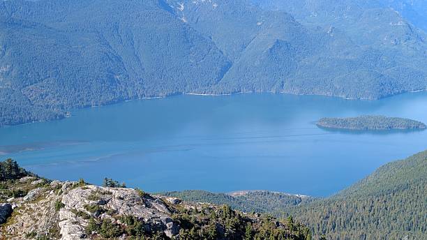 istock Pitt Lake surrounded by Forested Mountains, Snow-Capped Peaks, and Rocky Foreground Under Partly Cloudy Sky 2240208528