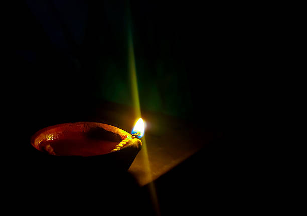 A traditional clay oil lamp (diya) with a burning cotton wick glowing softly in the dark, symbolizing hope, devotion, and the triumph of light over darkness in Hindu culture and festivals like Diwali.